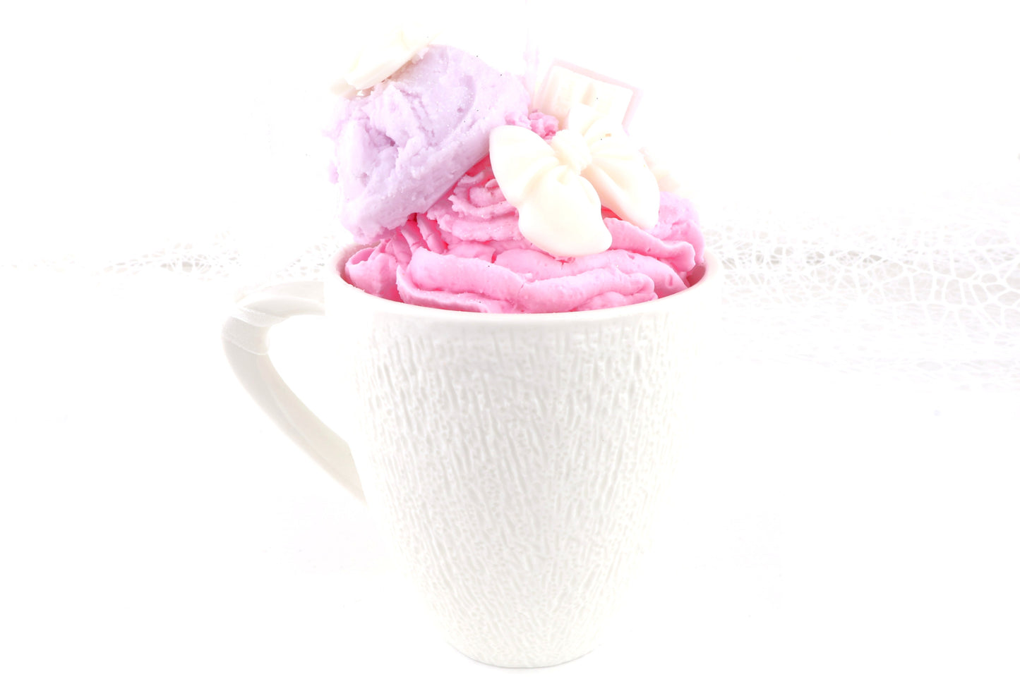 Pink-lila Dessertkerze in einer weißen Tasse, kunstvoll verziert mit Eiskugel und Schleifen – ideal als dekorative Duftkerze. 