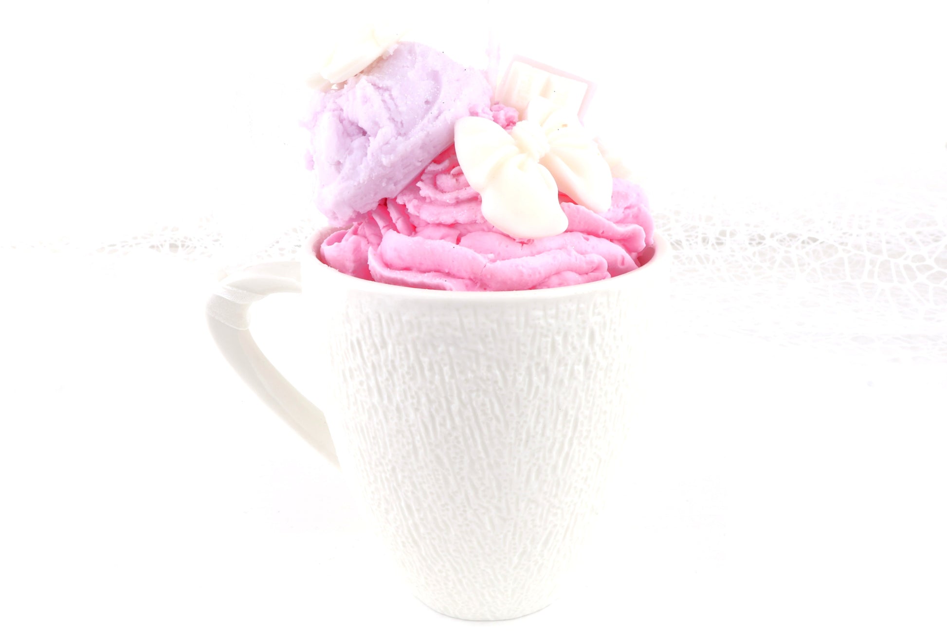 Pink-lila Dessertkerze in einer weißen Tasse, kunstvoll verziert mit Eiskugel und Schleifen – ideal als dekorative Duftkerze. 