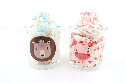 Zwei Dessertkerzen im Glas mit Löwen- und Giraffenmotiv, Sahneoptik, Glitzerdeko in Blau und Pink – liebevolle Deko für Kinderzimmer.