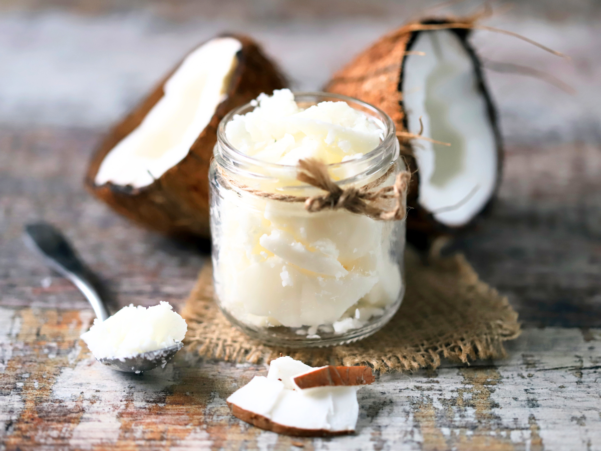 Frische Kokoscreme in einem Glas, umgeben von Kokosnussstücken und Löffel – natürliche Basis für Bio-Body-Peelings.