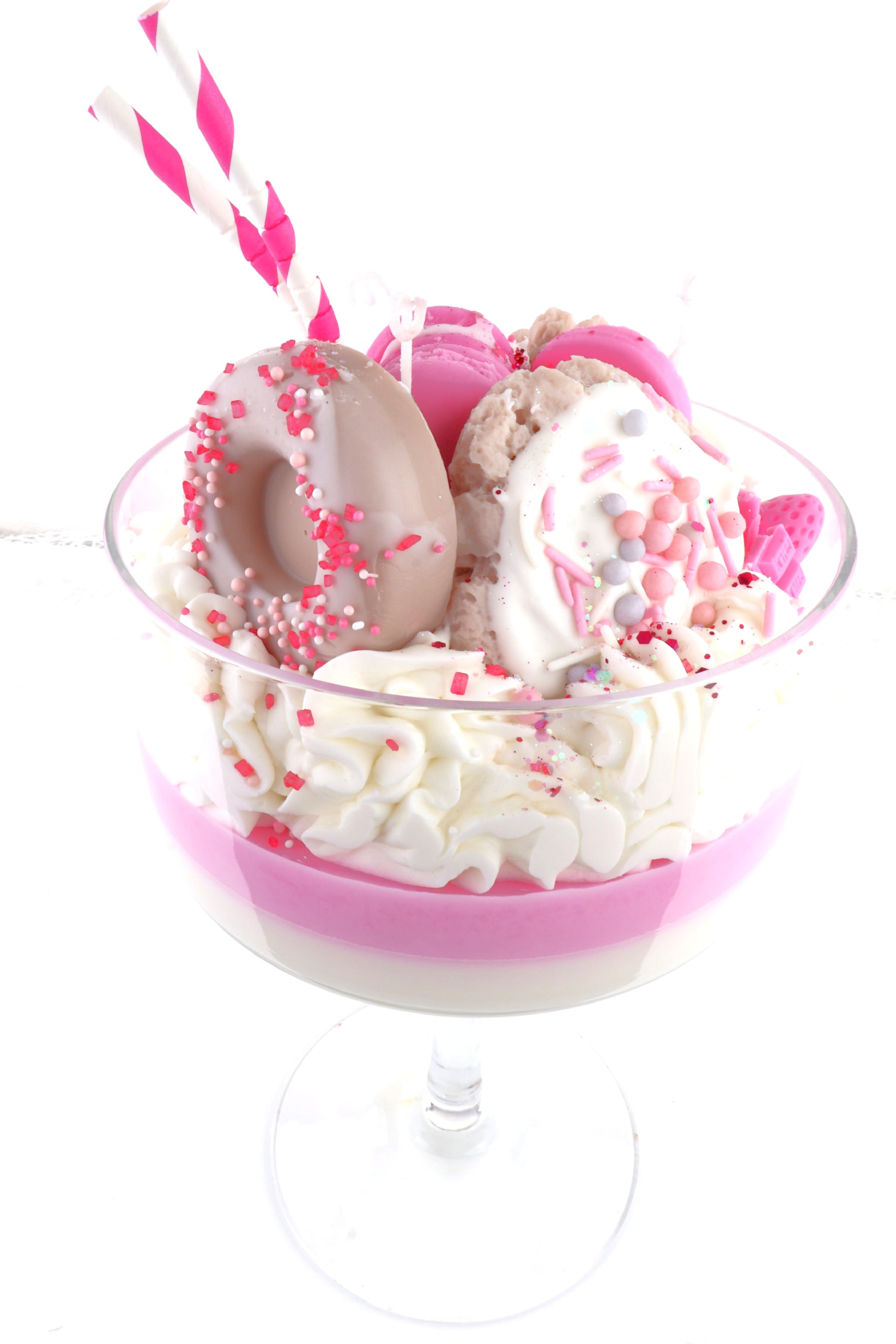 Pink weiß geschichtetes Dessert mit creme, Donutdeko, Macaron, Zuckersprinkles und gestreiften Strohhalmen im Champagnerglas.