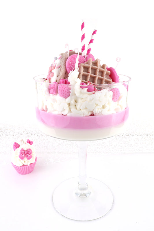 Big Pink weißes Dessert mit creme, Waffeln, suessen Dekoelementen und Streifenstrohhalmen im Champagnerglas.
