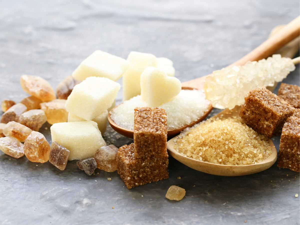 Verschiedene Zuckerarten wie Rohrzucker, Kandis und Würfelzucker auf Löffeln – natürliche Basis für Bio-Body-Peeling.